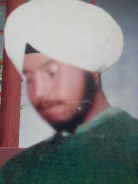 Grainy photo of victim Daljit Singh. He is a young Sikh man wearing a white turban and a green sweater. 